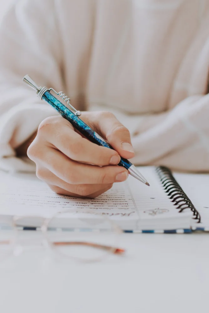 Mão fazendo anotações em um caderno, prática entre os encontros do intensivo de inglês