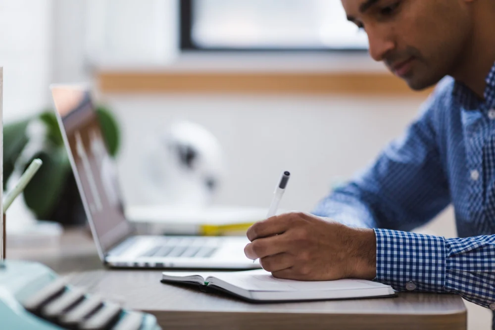 Profissional estudando no notebook e fazendo anotações durante o curso intensivo de inglês