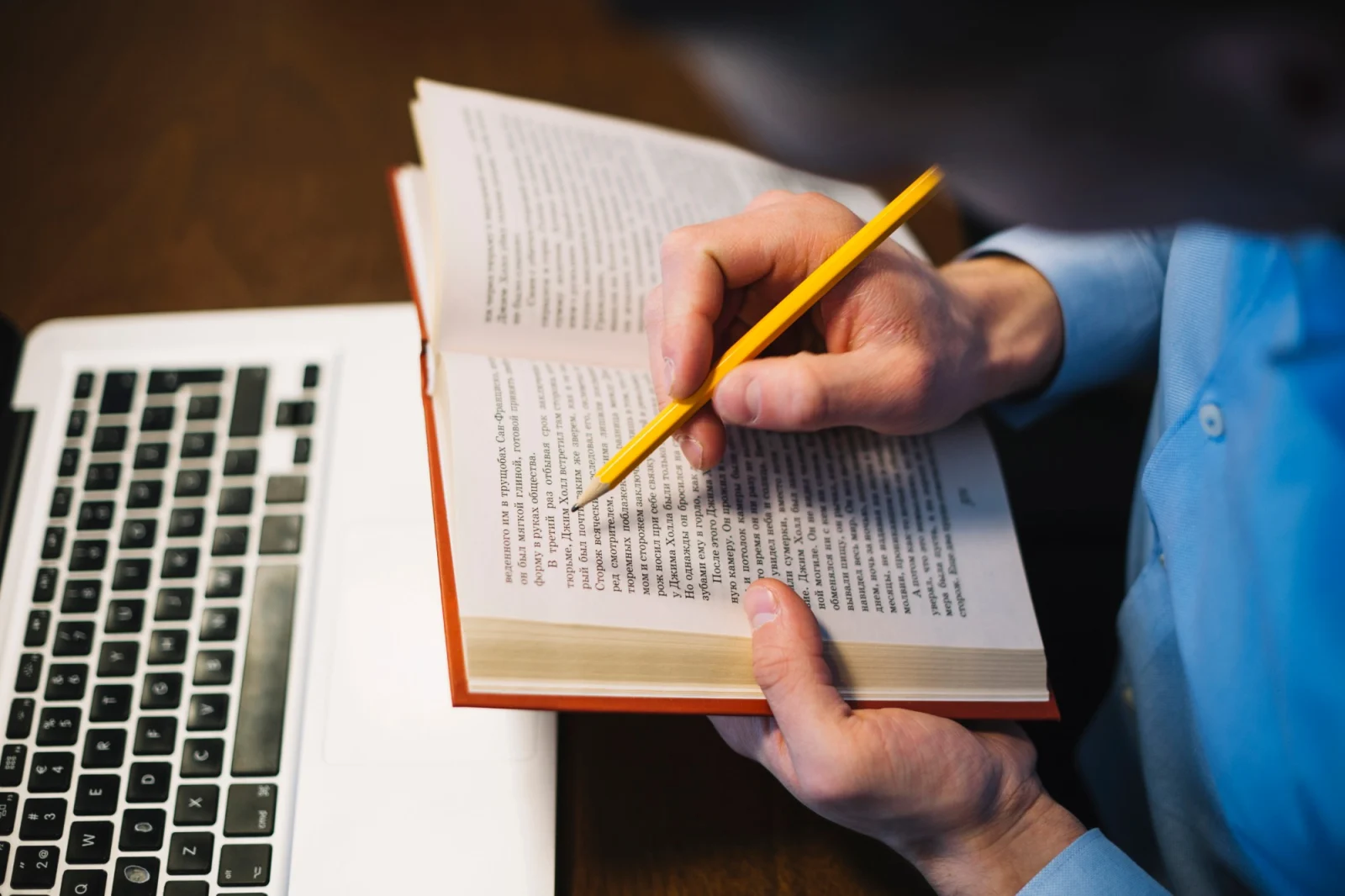 Estudante lendo um livro e fazendo anotações ao lado do notebook, estudo independente de inglês para iniciantes