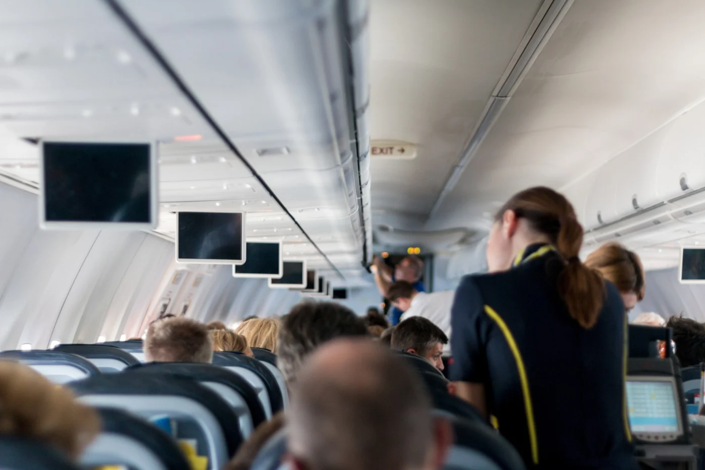 Comissária de bordo atendendo passageiros no corredor do avião, rotina que exige inglês para comissário de bordo