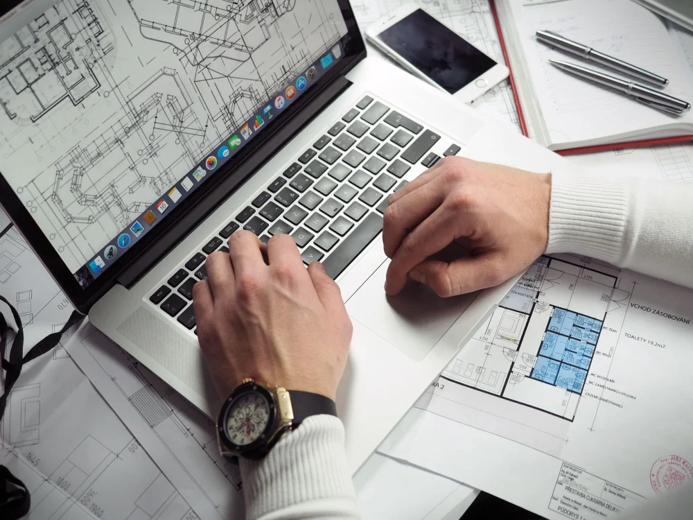 Engenheiro trabalhando no notebook com plantas e desenhos técnicos, profissional que desenvolve inglês para engenharia